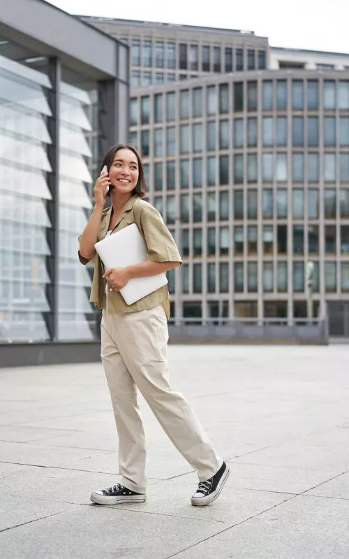 Vertical portrait of stylish asian girl student, talking on mobile phone while walking, holding